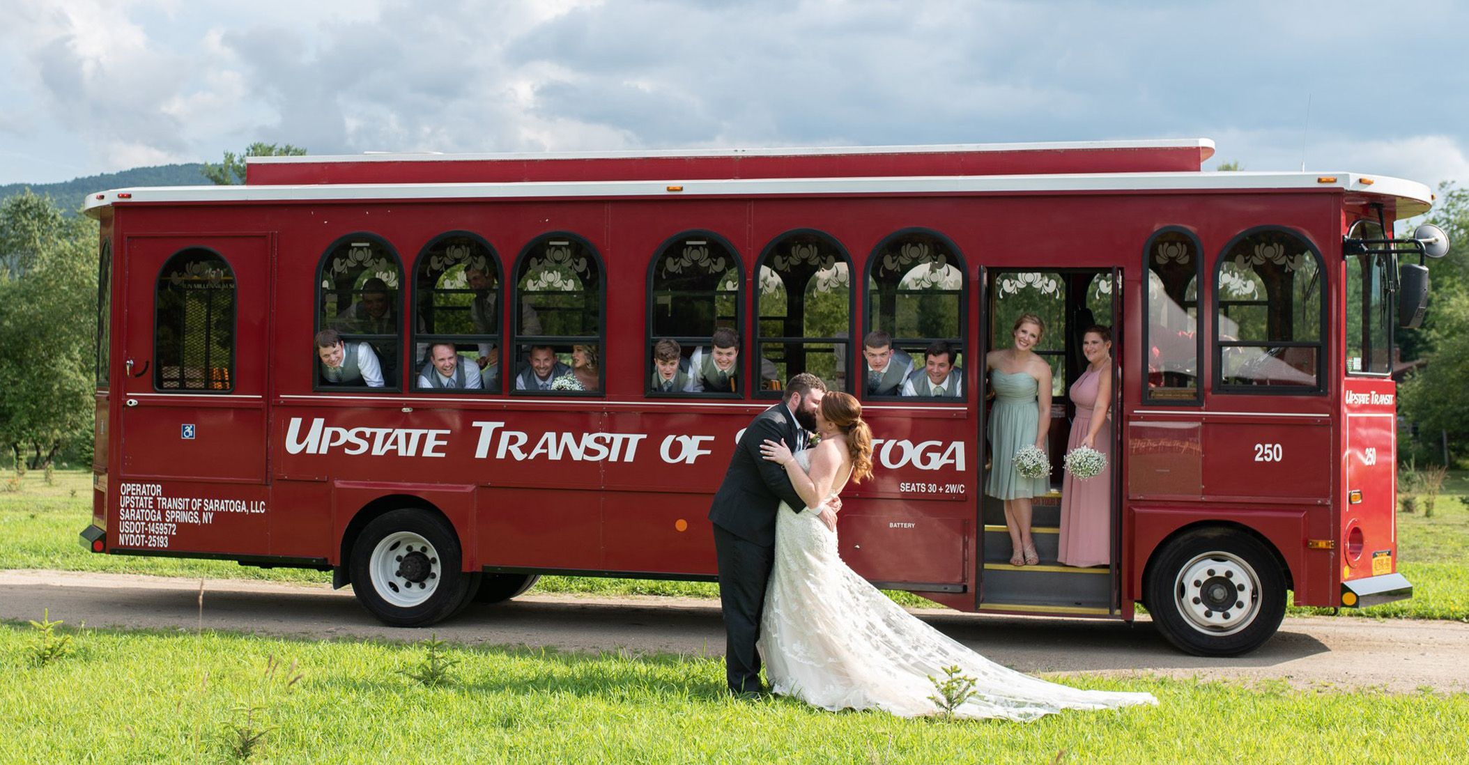a bride and a groom kissing in front of a trolley, with the bridesmaids and groomsmen watching them from on the trolley