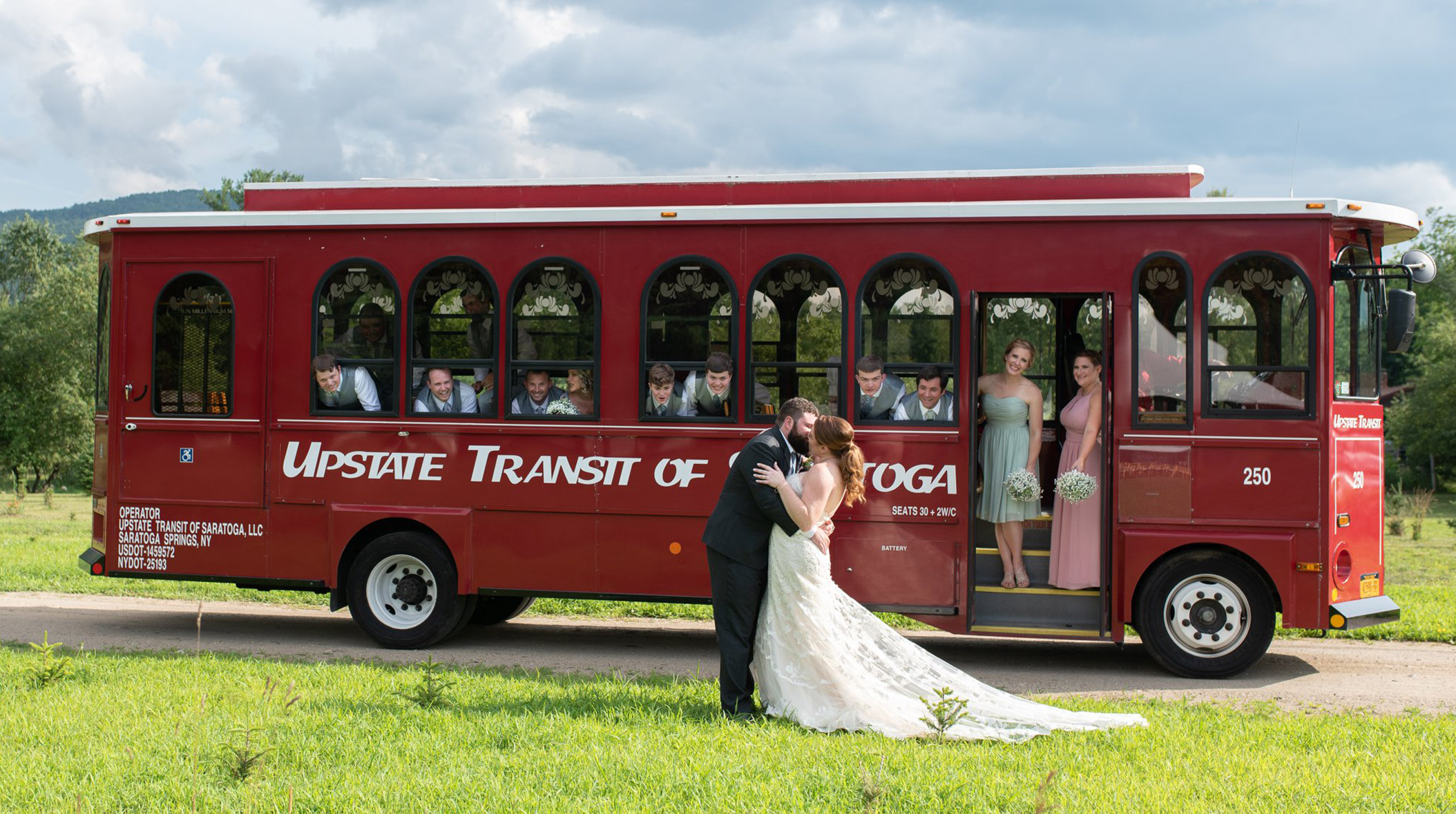 a bride and a groom kissing in front of a trolley, with the bridesmaids and groomsmen watching them from on the trolley